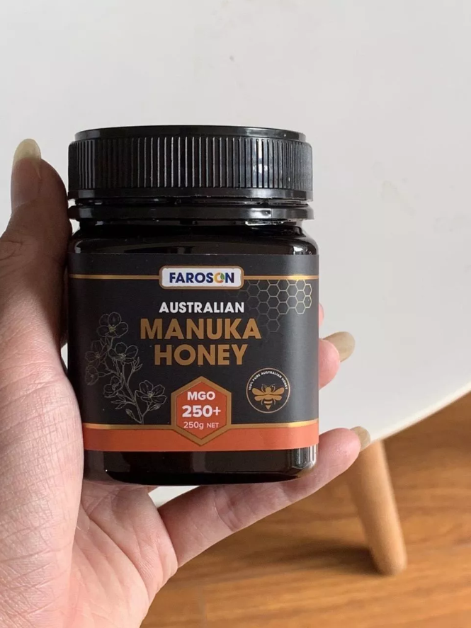 Jar of Farason Australian Manuka Honey held by a hand on a wooden surface.